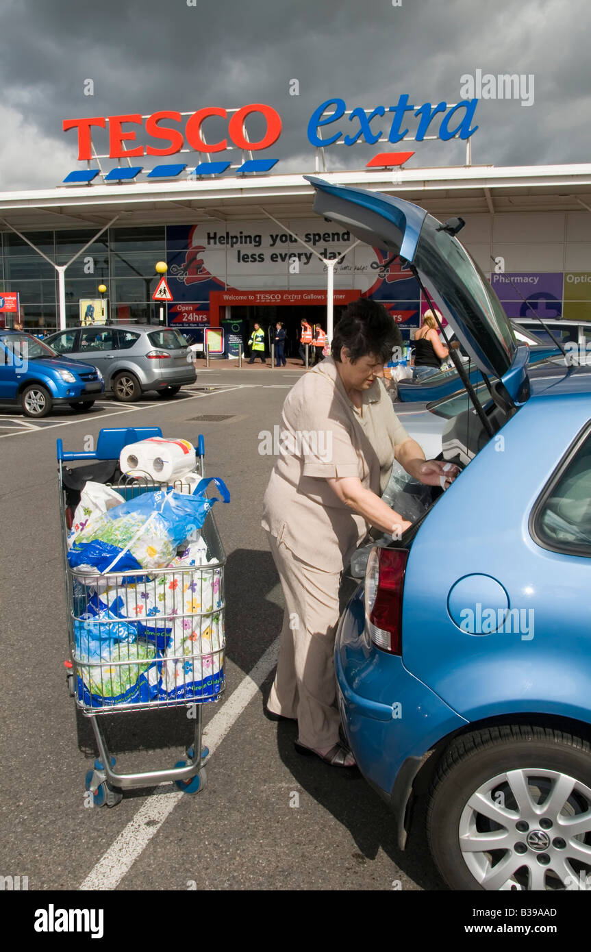 Tesco Extra supermarket store car park mature woman shopper loading weekly grocery food shopping into car from trolley Romford London England UK Stock Photo