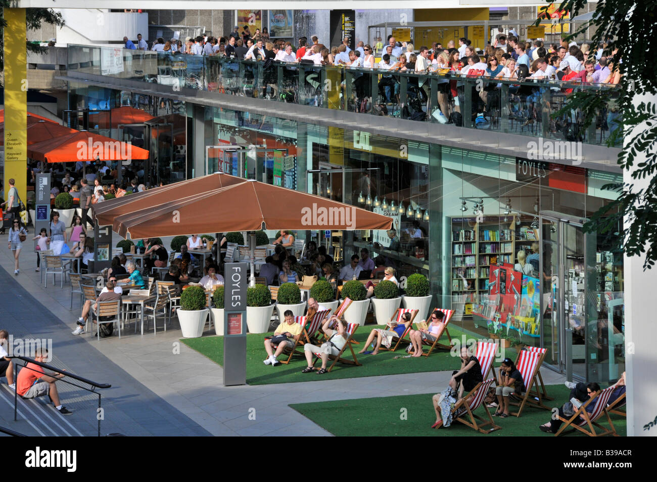 Summer lunch time people at Foyles bookshop in deckchairs & on Royal Festival Hall terrace at the riverside South bank beside River Thames London UK Stock Photo