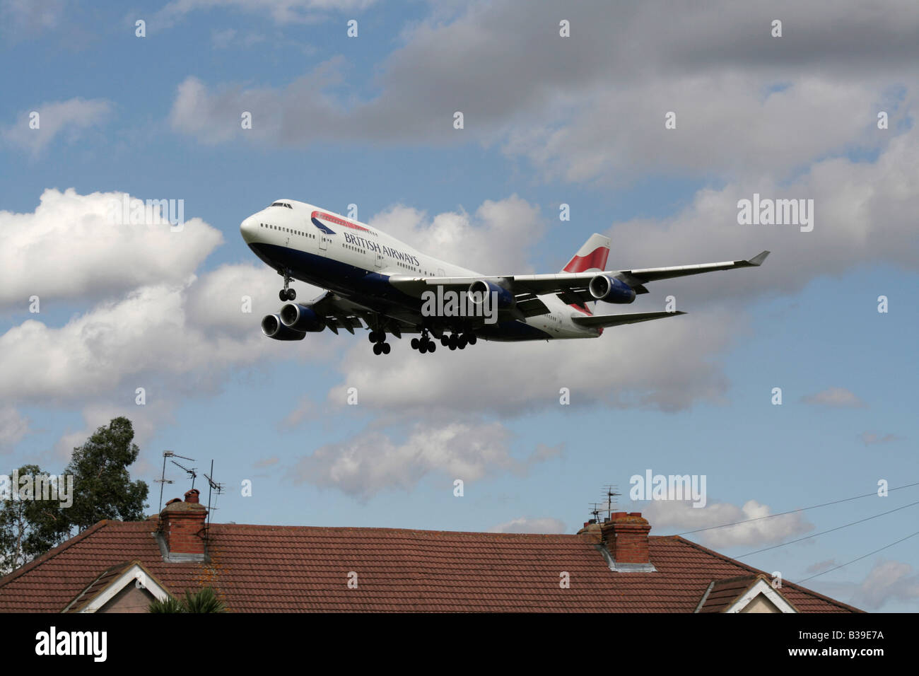British Airways Boeing 747-400 passenger jet airliner overflies a house while on approach to Heathrow Airport. Civil aviation and noise pollution. Stock Photo