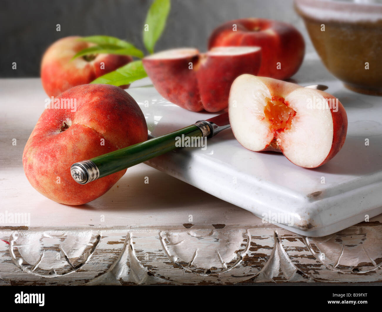 Still life of fresh donut peaches, cut and whole in a rustic kitchen setting Stock Photo
