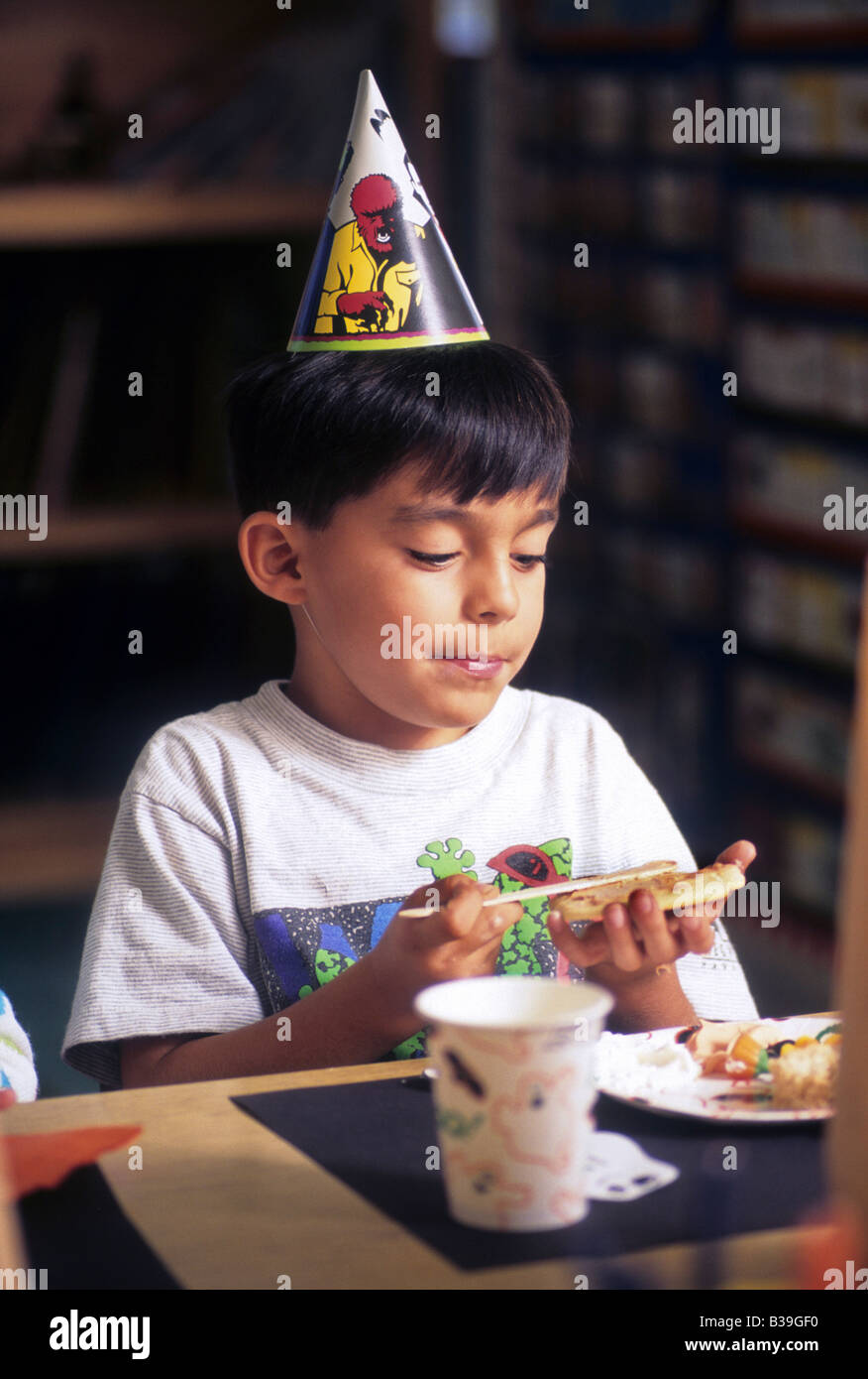 Seven-year old Hispanic boy eats treat at birthday party. Stock Photo