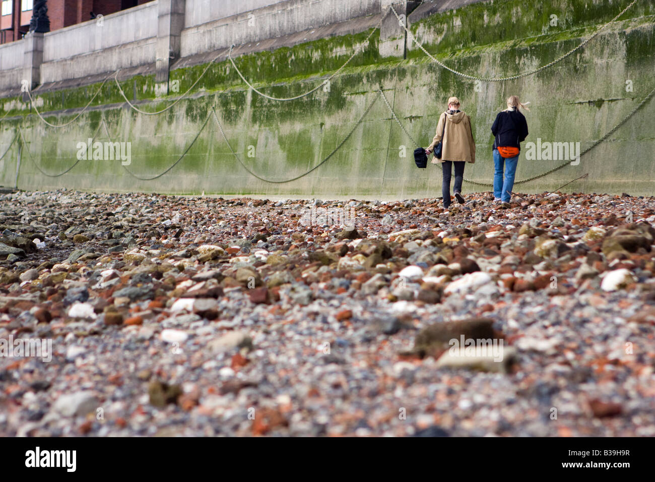 Two women walking along the shoreline of The Thames in London, UK Stock Photo