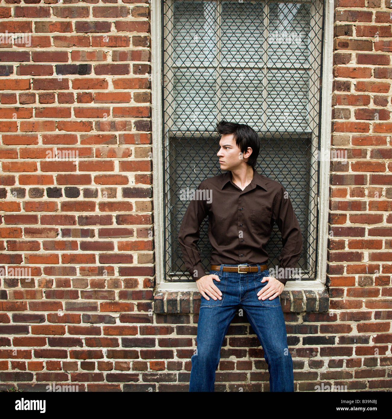 Asian man standing and leaning against window and brick wall Stock Photo