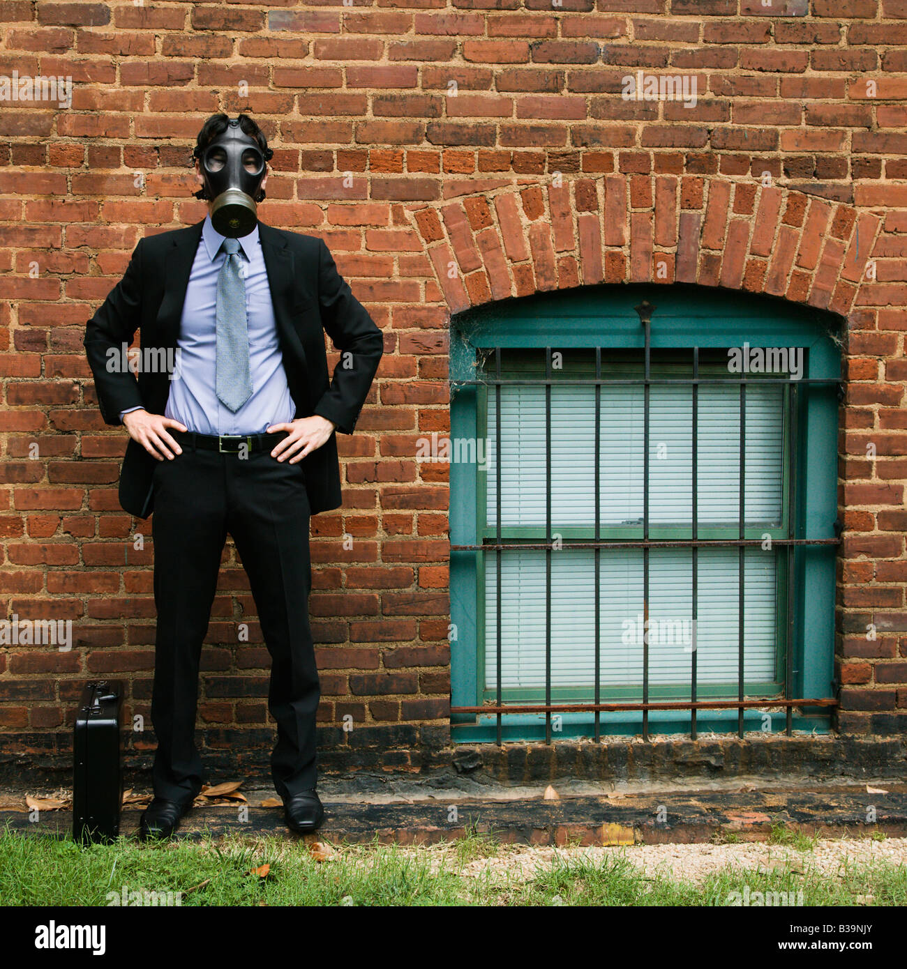 Businessman standing next to brick wall wearing gas mask Stock Photo