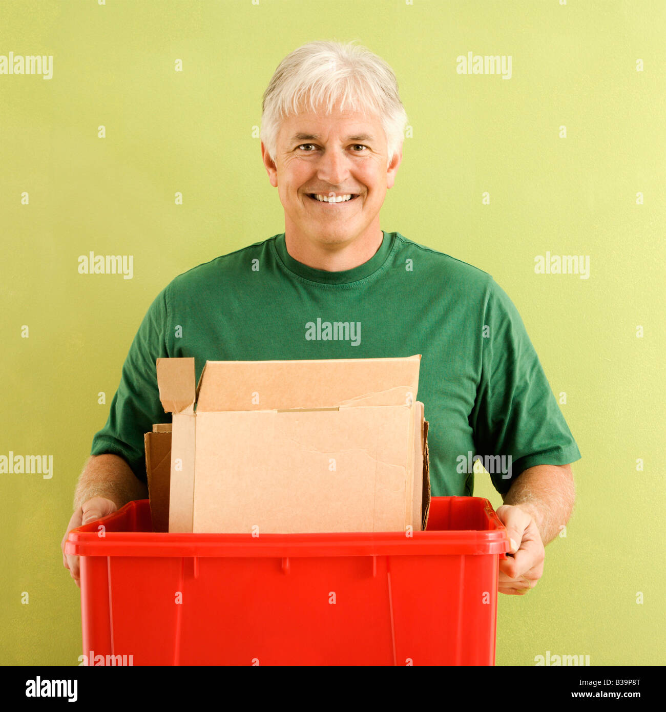 Portrait of smiling adult man holding recycling bin full of cardboard Stock Photo