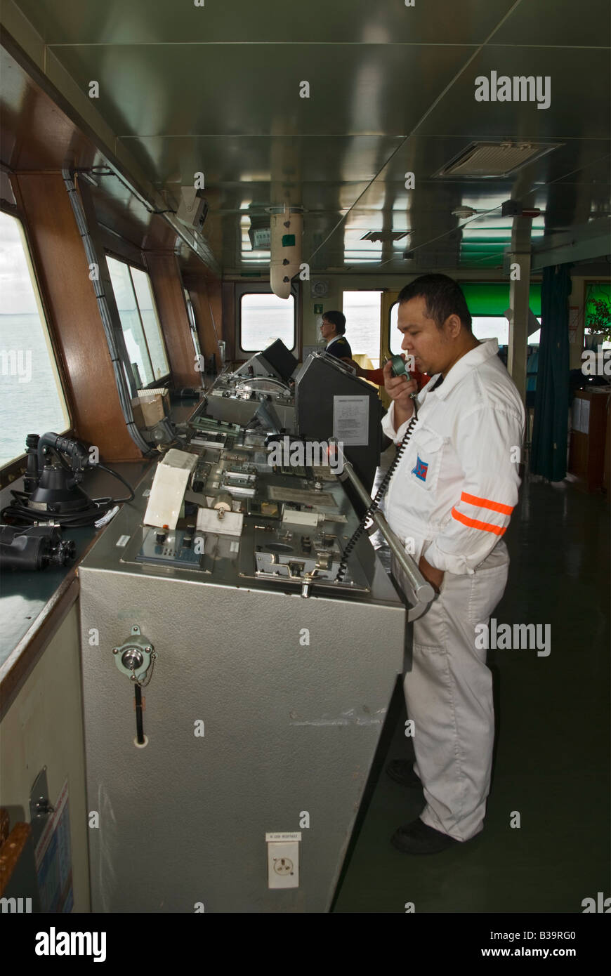 A crew member of a ship entering port holds a microphone while making a call on the ship's public address system. Stock Photo
