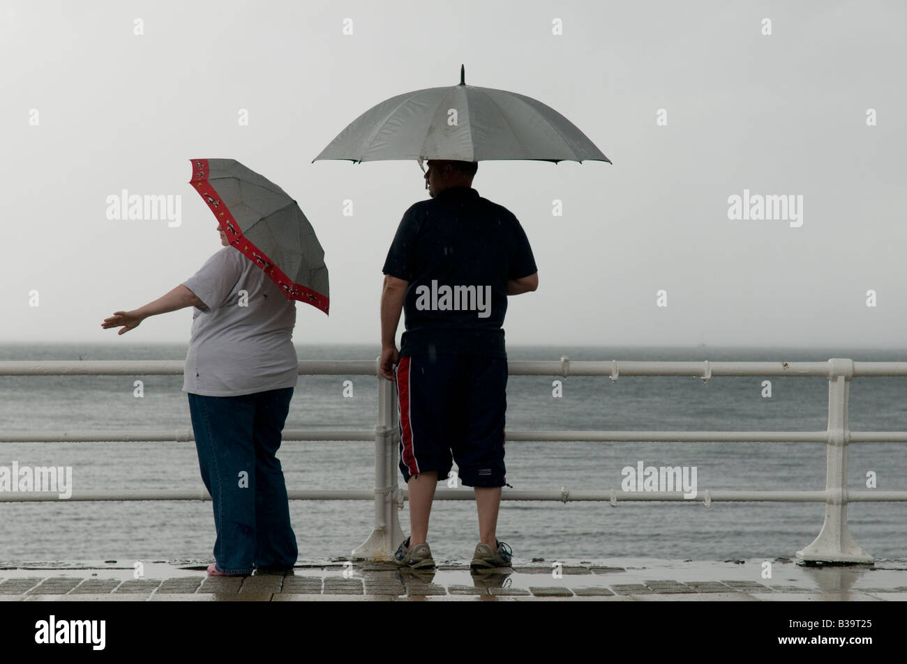 Two people standing in the rain under umbrellas on Aberystwyth seaside promenade August 2008 - wet and windy bad summer weather Stock Photo