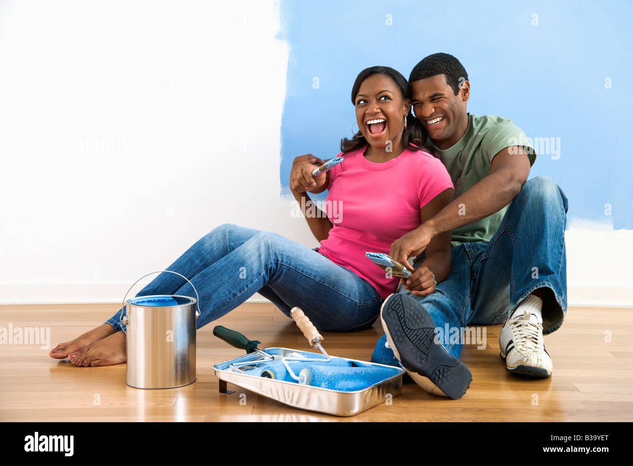 African American couple sitting together relaxing next to half painted wall and painting supplies Stock Photo