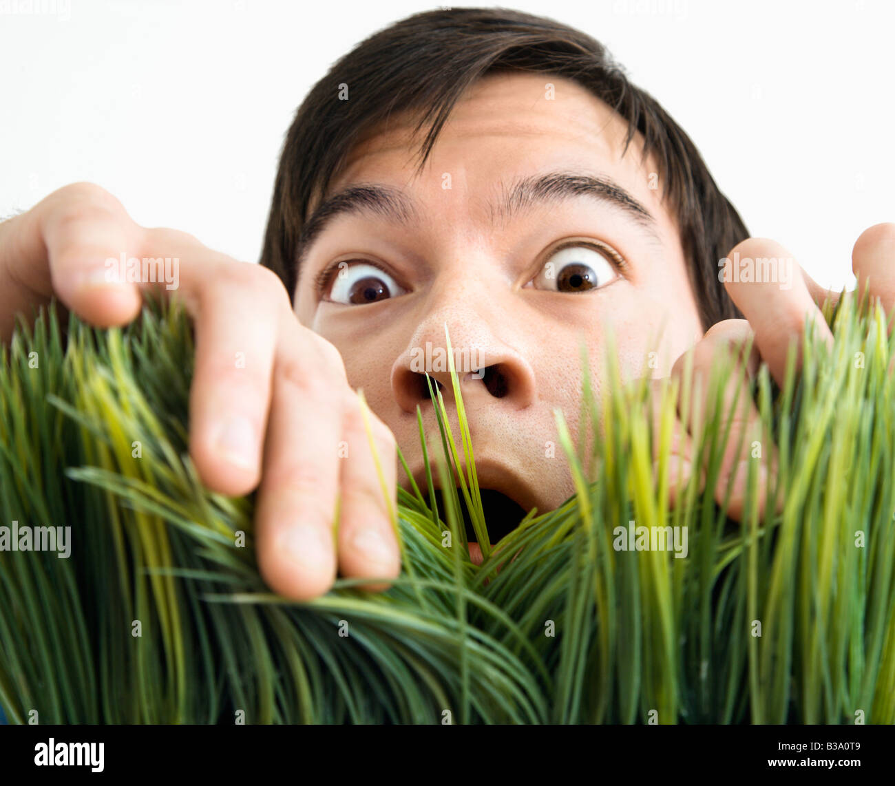 Asian young man looking through grass with fearful expression Stock Photo