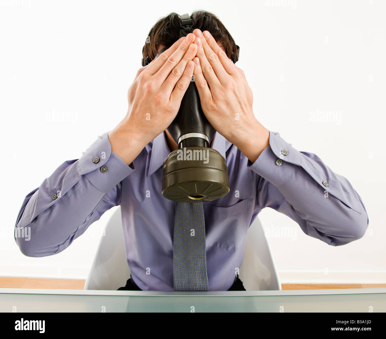 Businessman sitting wearing gas mask holding his hands over his eyes Stock Photo