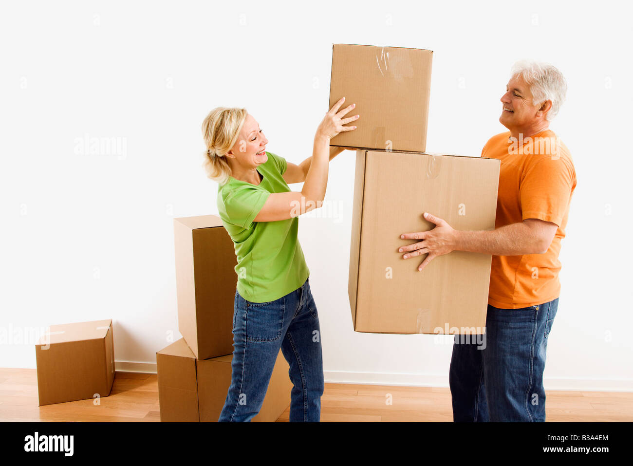 Middle aged man holding cardboard moving boxes while woman places one on stack Stock Photo