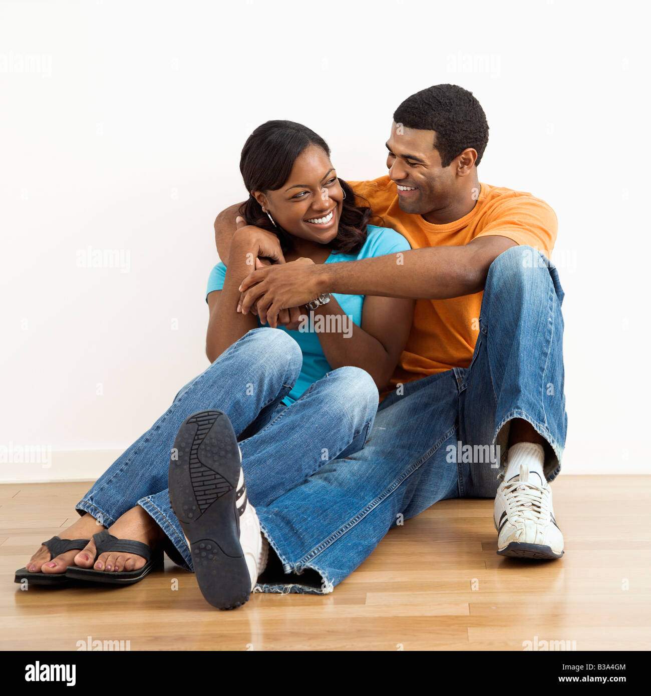 Happy smiling African American couple sitting on floor snuggling Stock Photo
