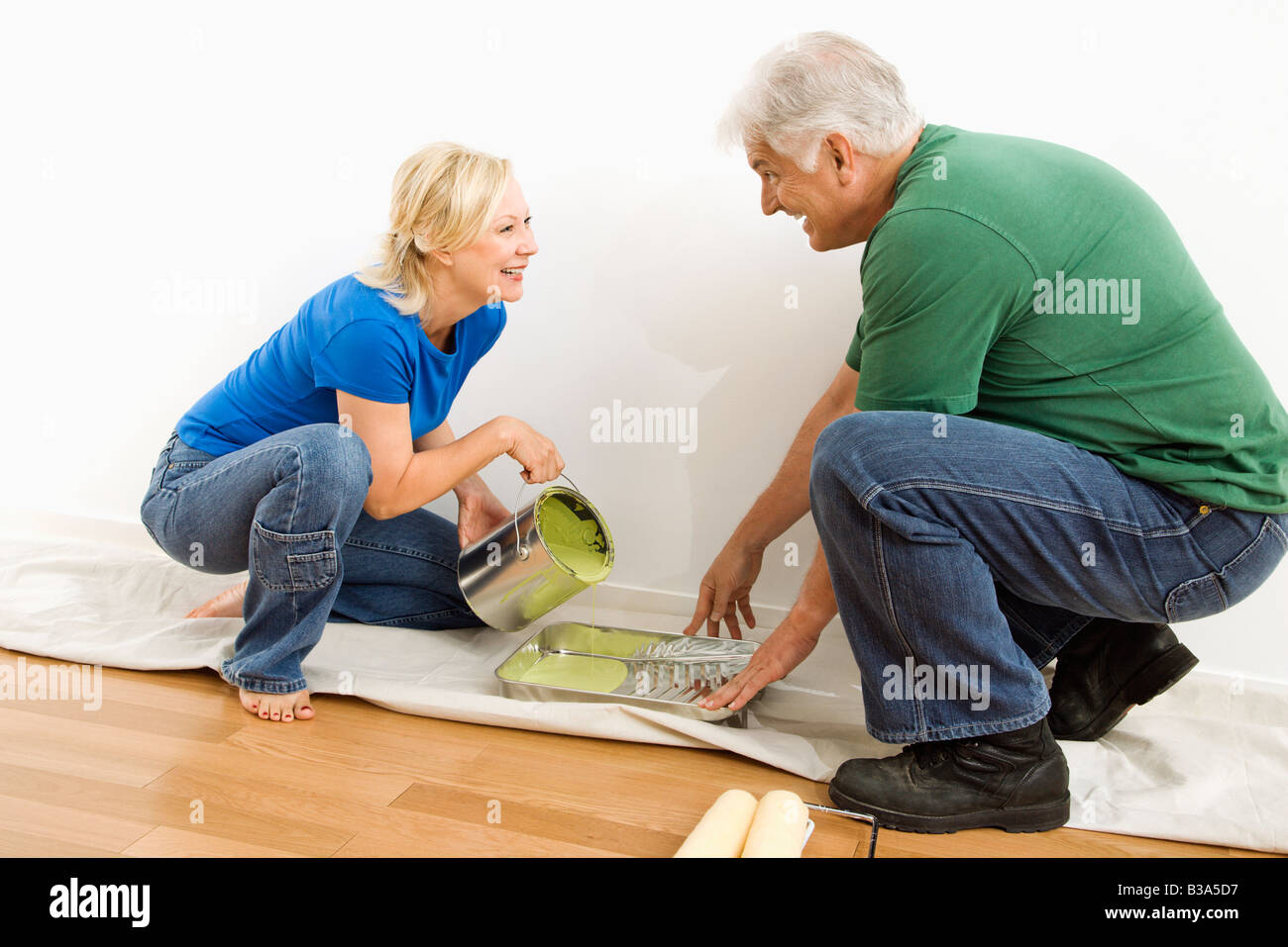 Middle aged couple pouring paint into tray on drop cloth Stock Photo
