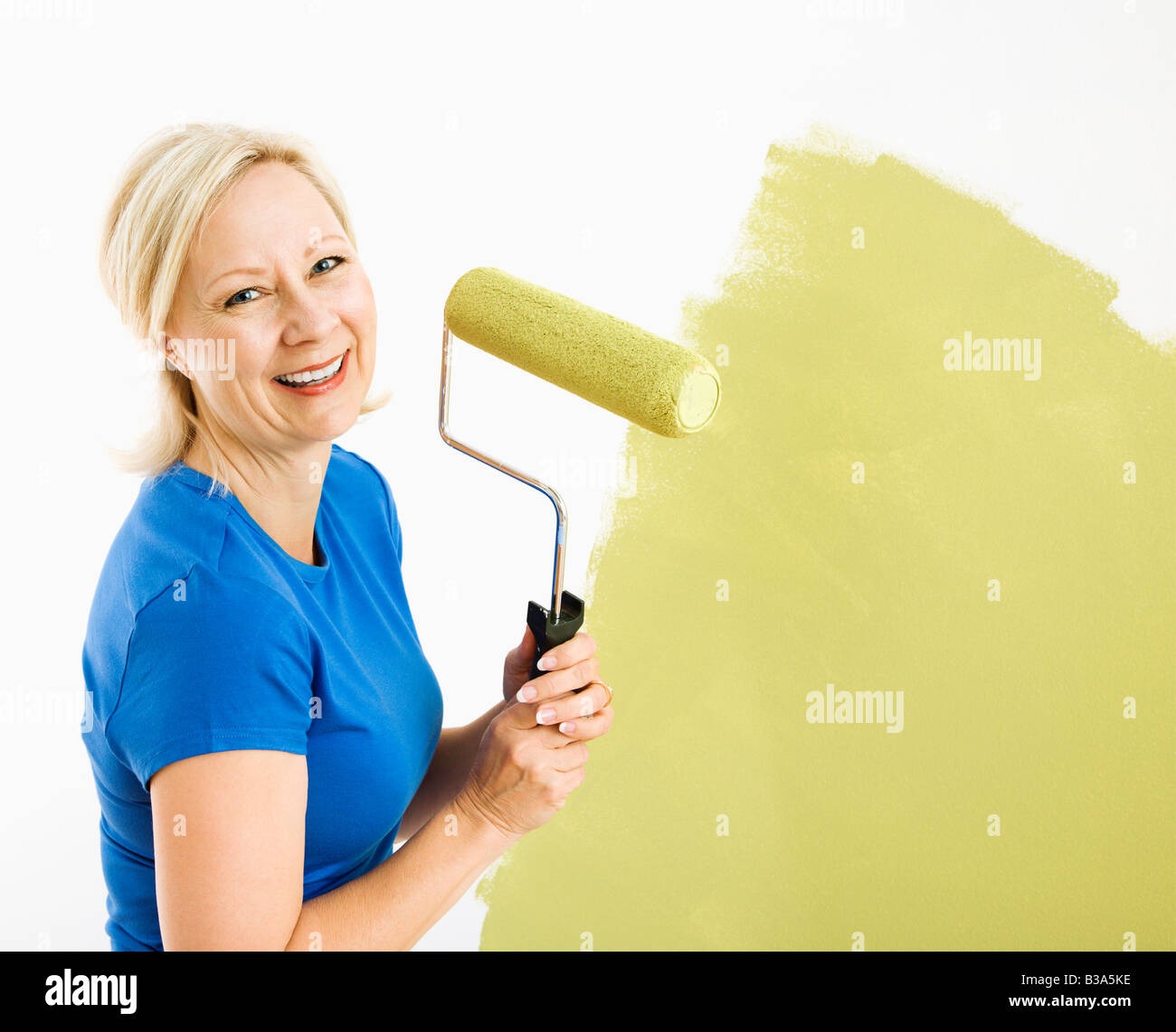 Middle aged woman painting wall green with paint roller smiling at viewer Stock Photo