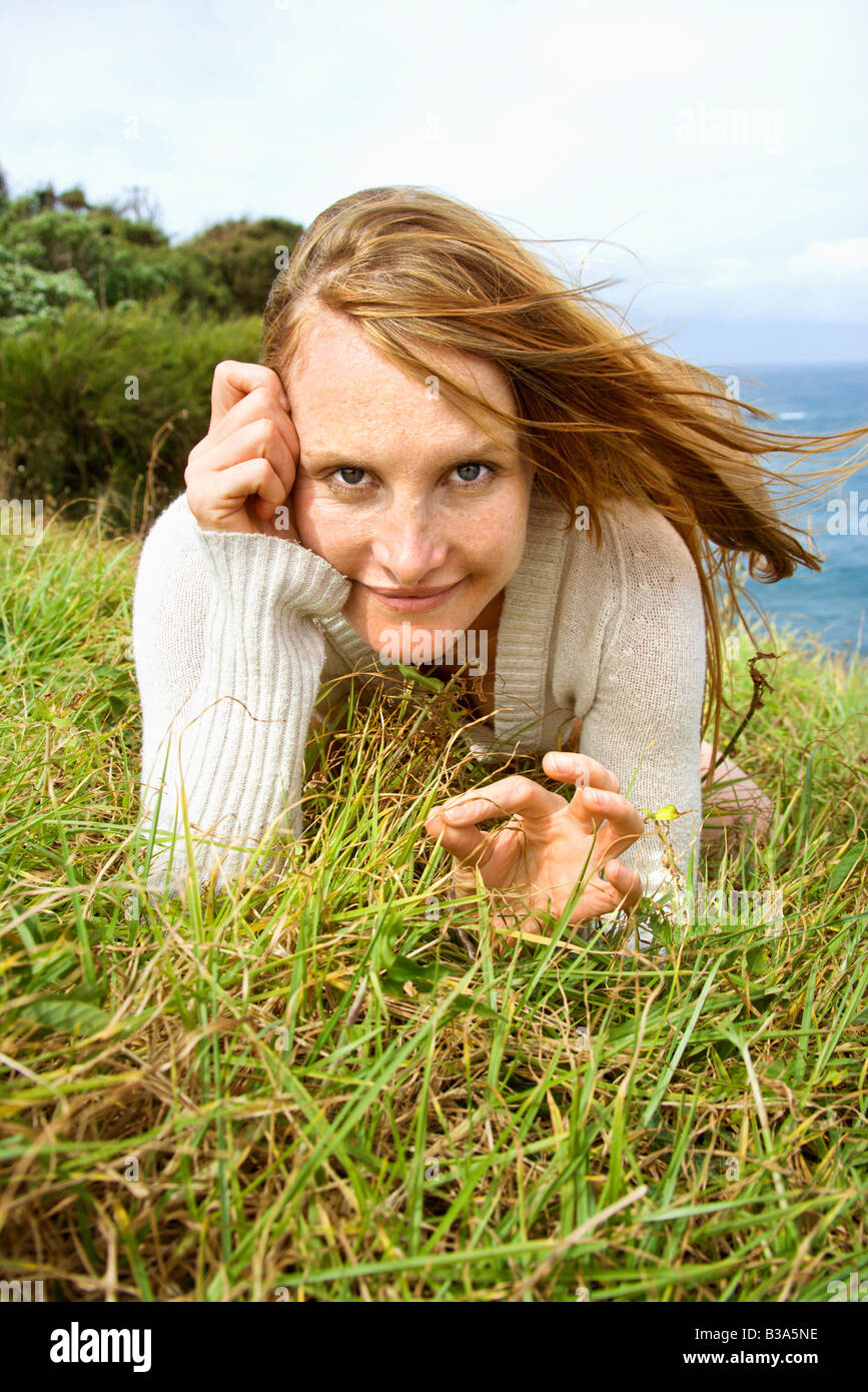 Portrait of young redheaded woman lying in grass looking at viewer with devilish grin Stock Photo