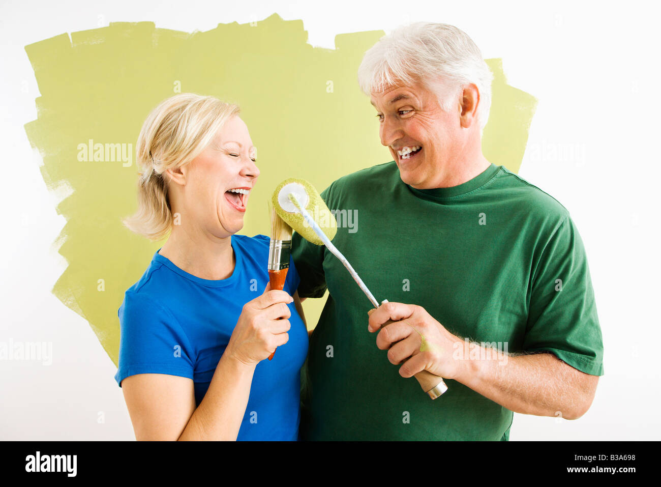 Middle aged couple painting wall green playing with paint utensils Stock Photo