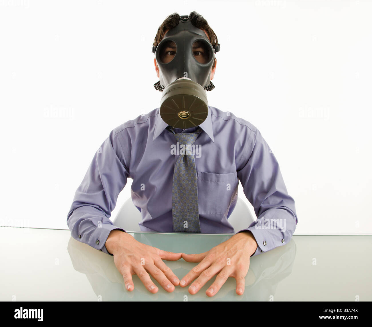 Businessman sitting in white room wearing gas mask Stock Photo