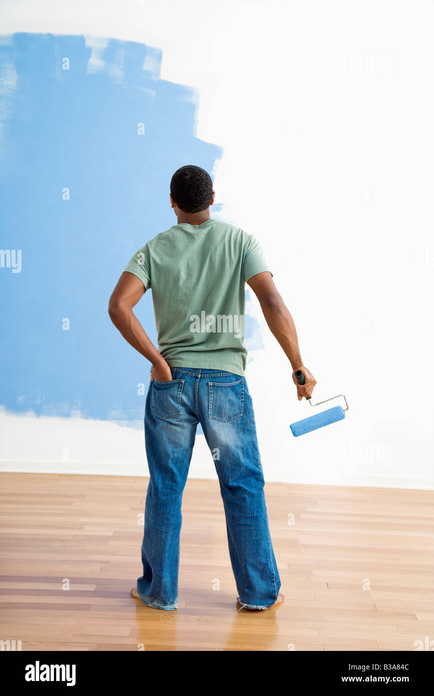 African American young man standing next to half painted wall with paint roller Stock Photo