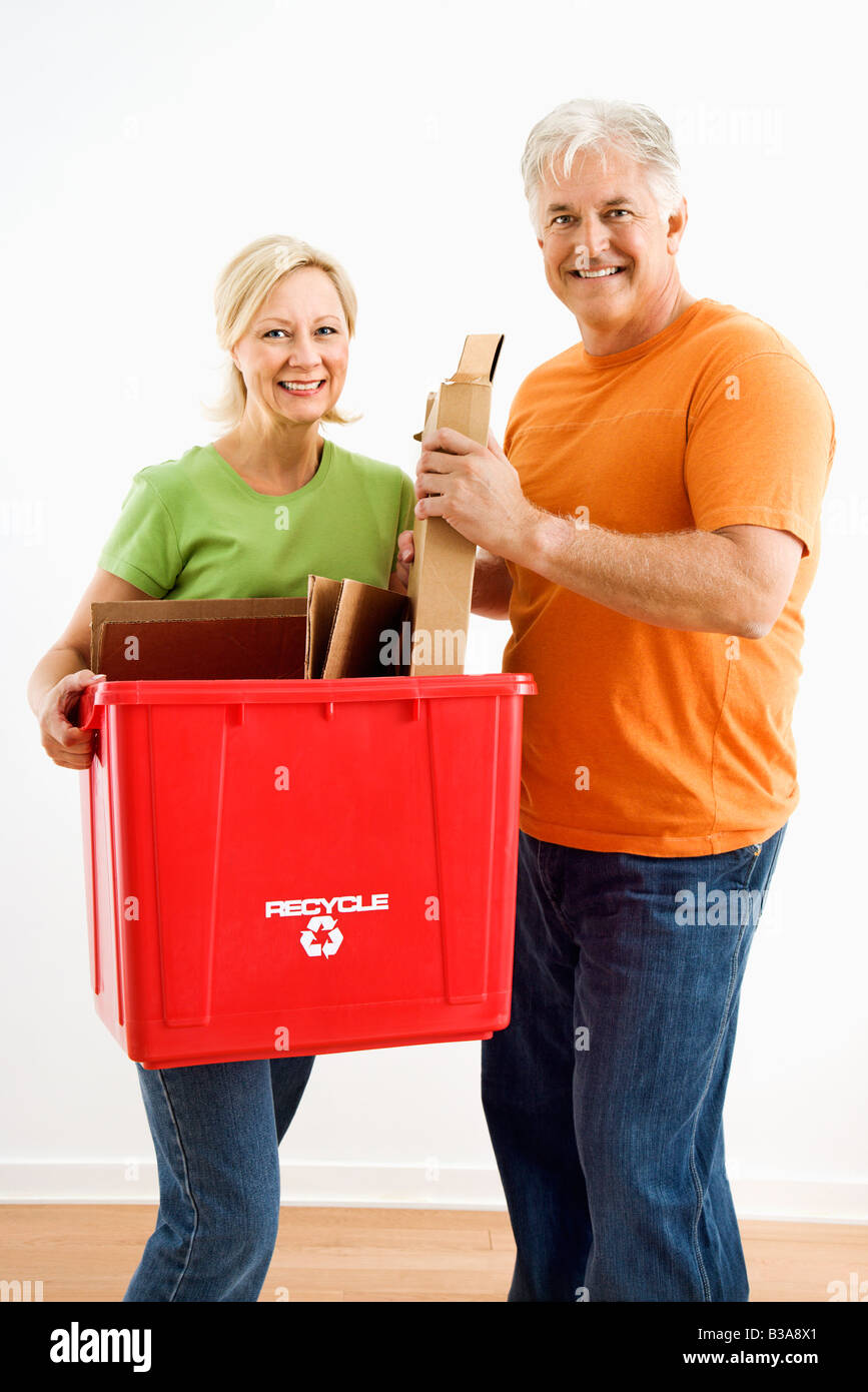Man and woman smiling while holding recycling bin Stock Photo
