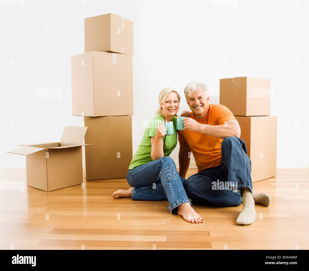 Middle aged couple sitting on floor among cardboard moving boxes with coffee Stock Photo