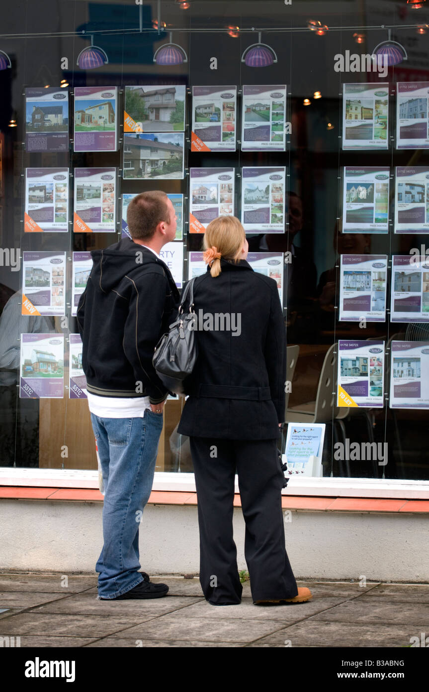Young couple first time buyers at estate agent window checking property prices Stock Photo