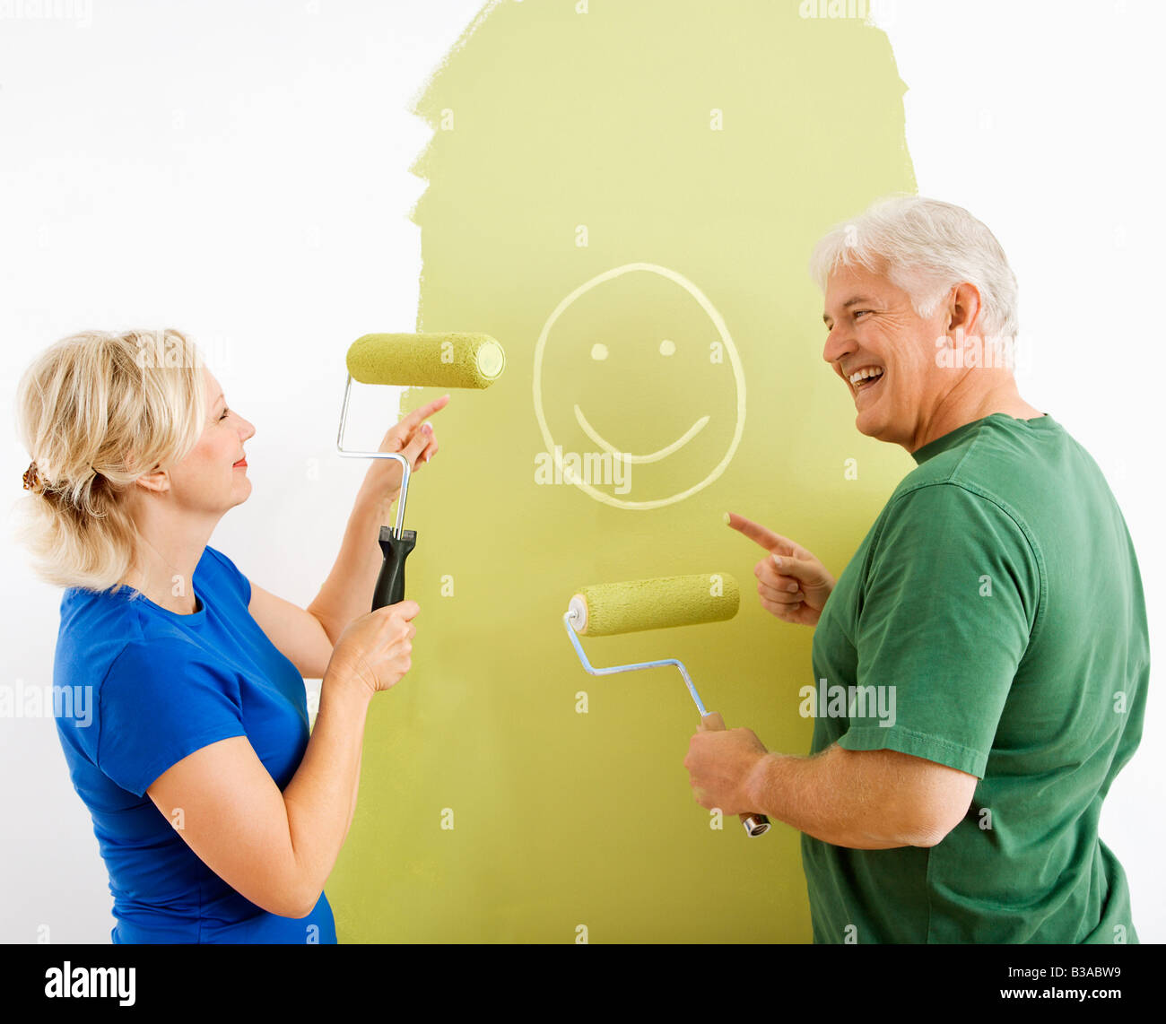 Middle aged couple painting wall green finger painting smiley face for fun Stock Photo