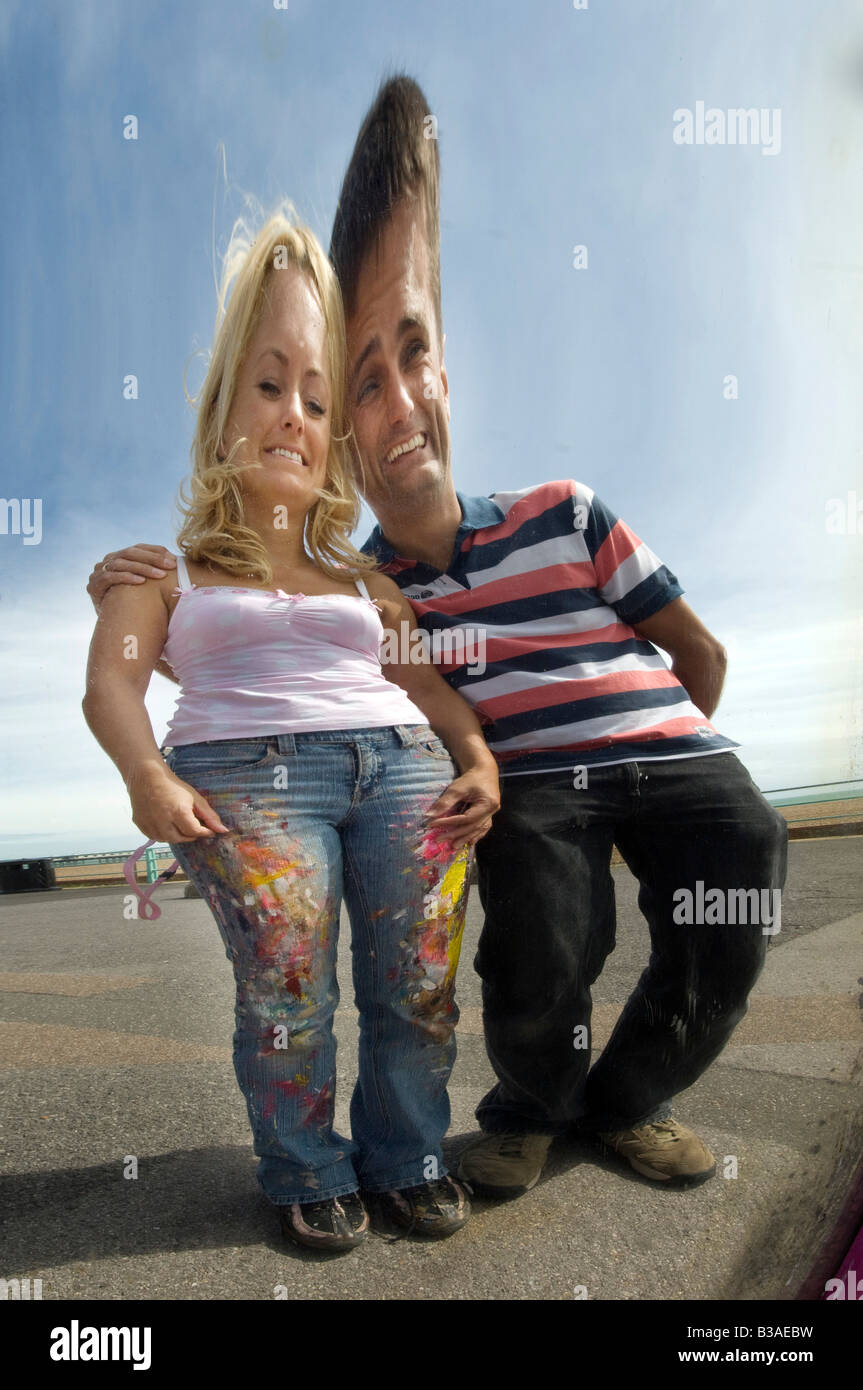 A young couple laugh at their images in an old fairground distorting mirror on Brighton seafront Stock Photo