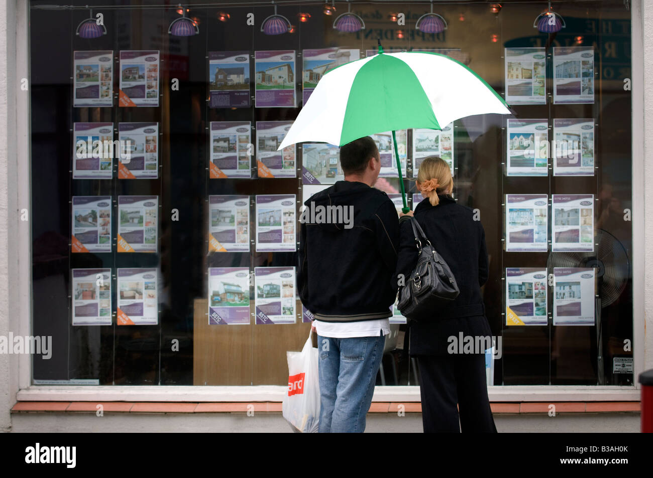 Young couple first time buyers at estate agent window checking property prices Stock Photo