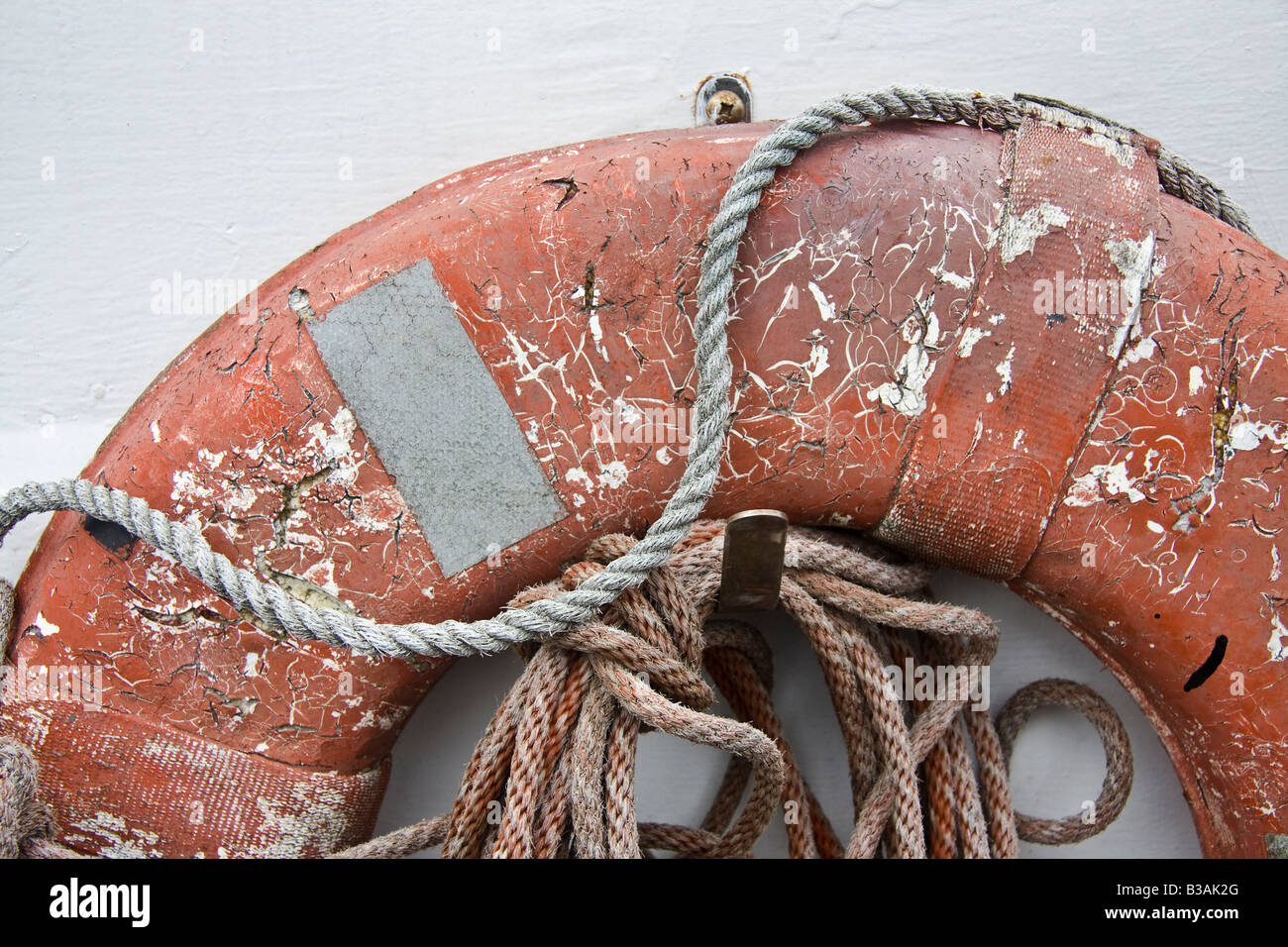weathered orange life buoy with rope against a white wall Stock Photo ...