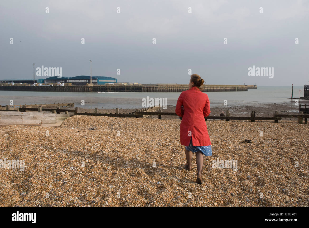 Woman walk on beach wearing a red coat in stormy weather Stock Photo