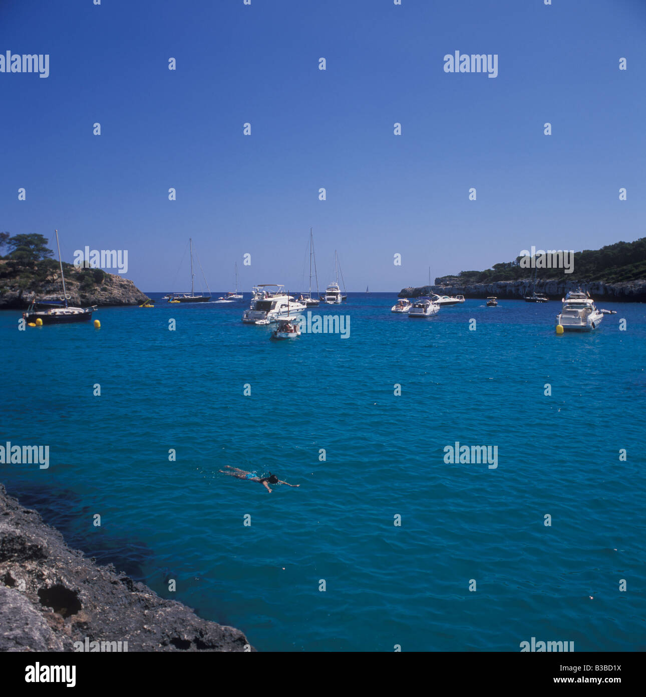 Scene in Cala Mondrago - swimmer + boats and yachts at anchor looking seawards - near Cala D'Or, East Coast Mallorca. Stock Photo