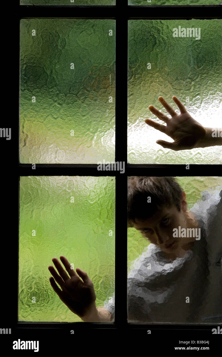 silhouette of person behind glass window with hands on panes of glass Stock Photo