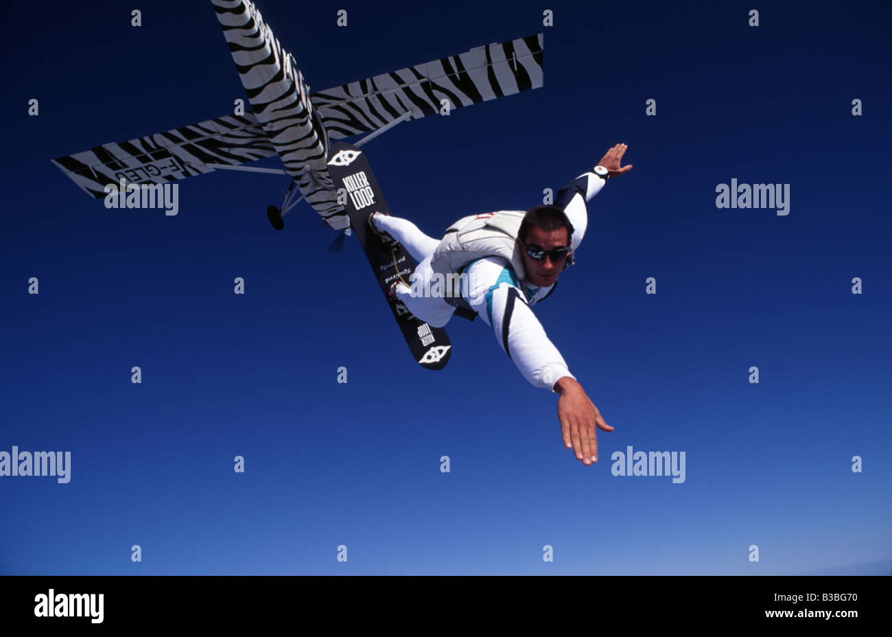 A skysurfer exits an zebra coloured airplane on a surfboard Stock Photo