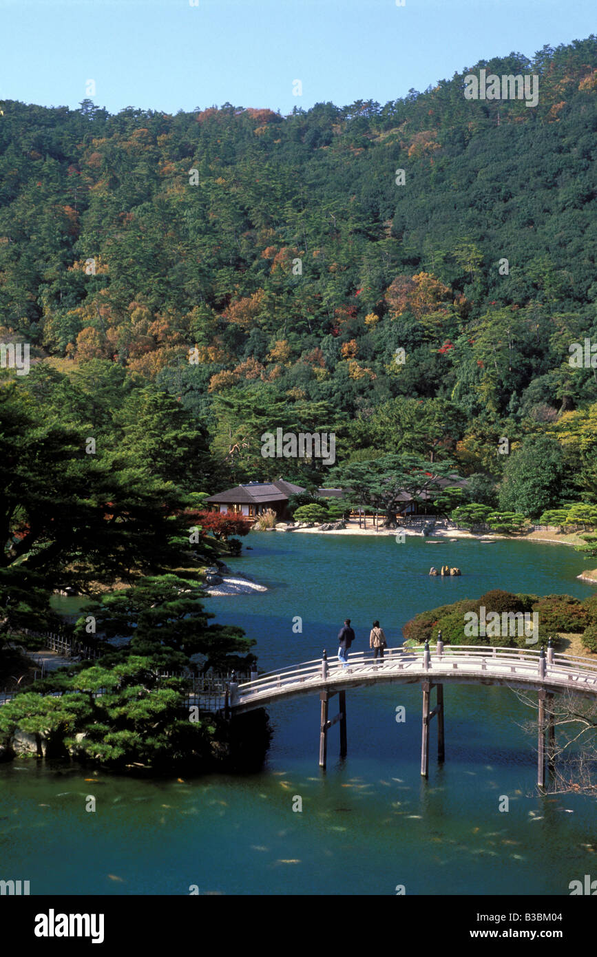 Visitors to the famous Ritsurin Koen landscape garden in Takamatsu pause atop an arched bridge to appreciate the koi fish below Stock Photo
