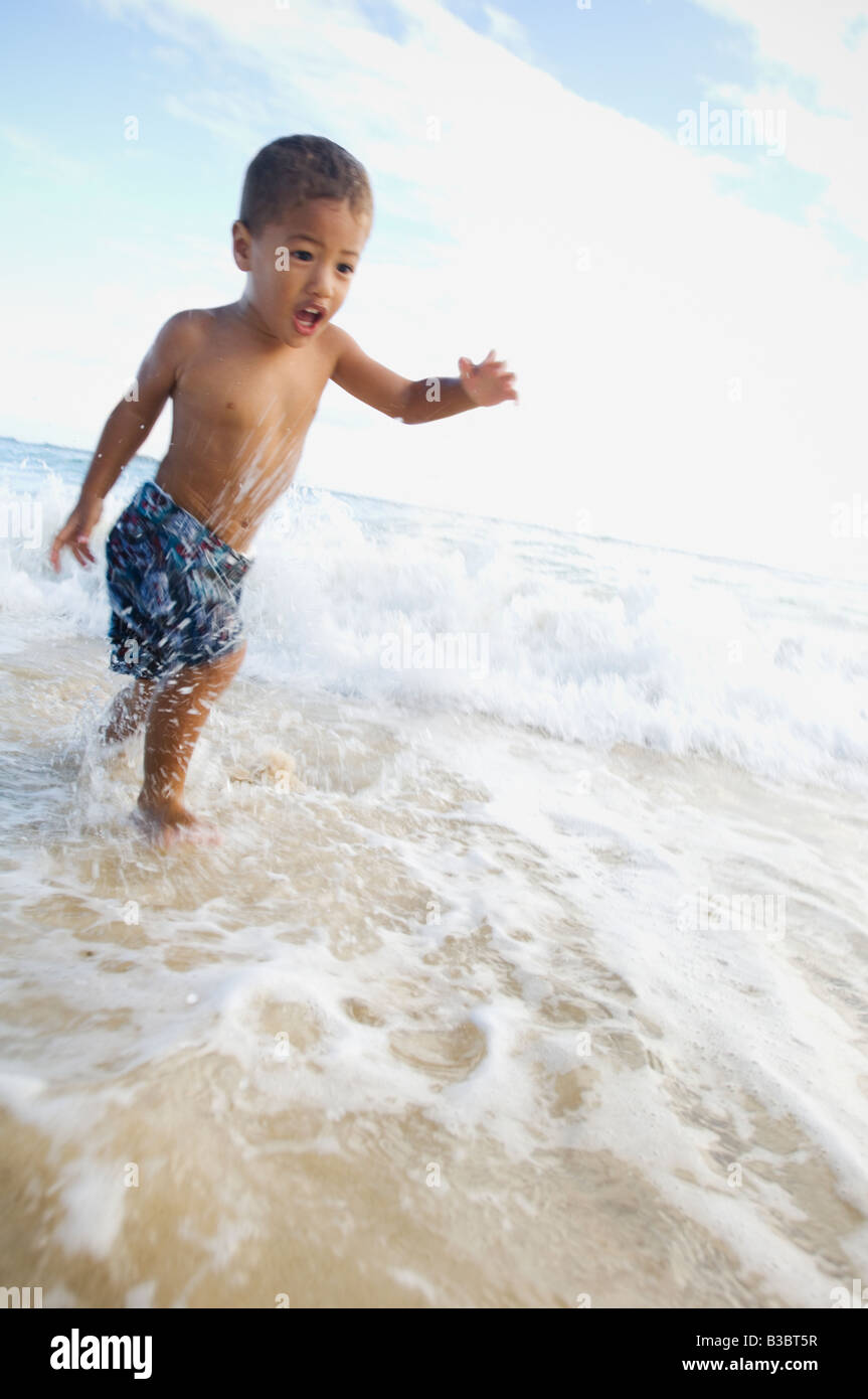 Pacific Islander boy wading in ocean surf Stock Photo
