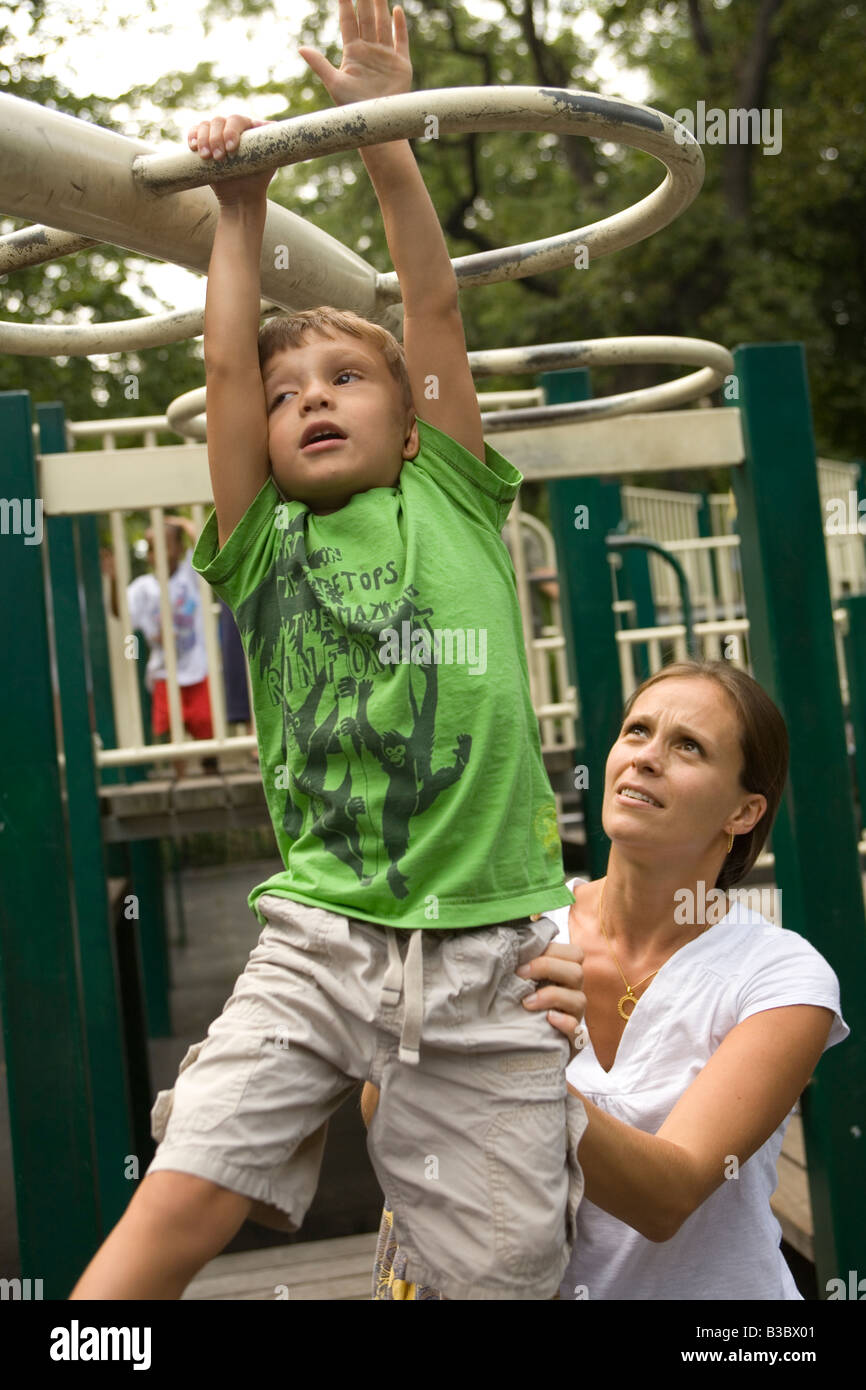 Four year old child building strength and confidence on the monkey bars with his mother nearby Stock Photo