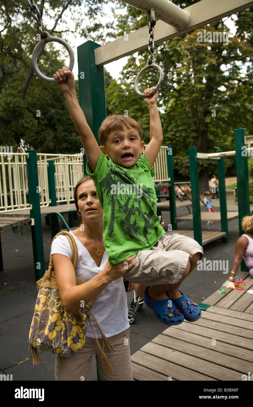 Four year old child building strength and confidence on the monkey bars with his mother nearby Stock Photo