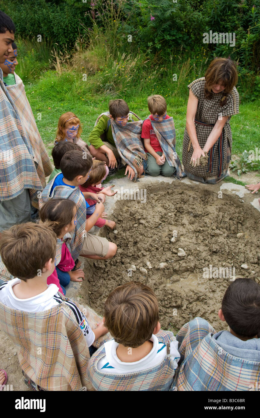 UK, Wales, Pembrokeshire. Children are shown how to gather mud to build wattle & daub walls by one of the guides at Castle Henllys, a recreated Iron Age Fort built on its original foundations near Newport. Stock Photo