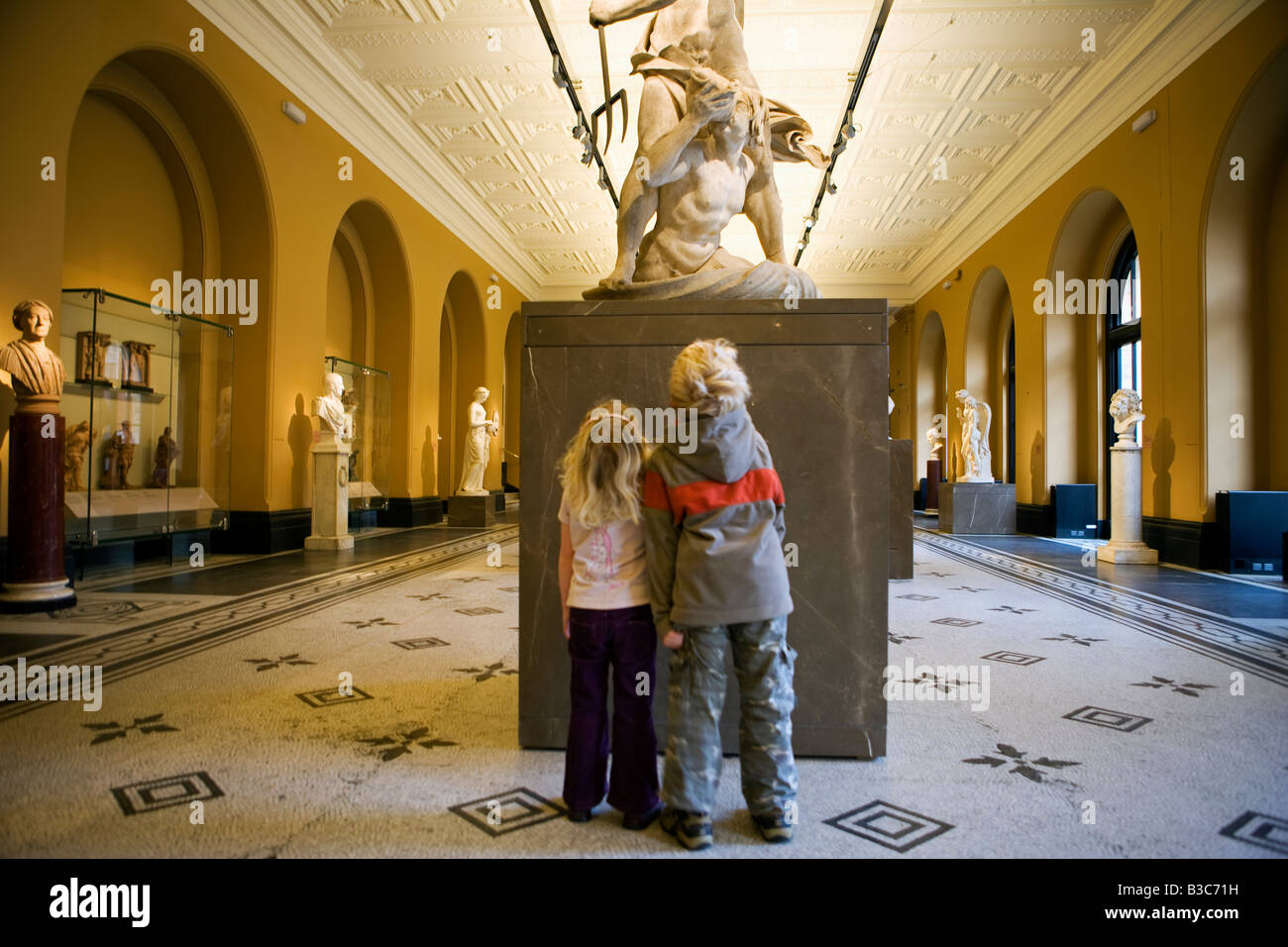 England, London, Victoria and Albert Museum. A brother and sister look up at a classically carved statue in the a viewing gallery of one of the world's most important visitor centres. (MR). Stock Photo