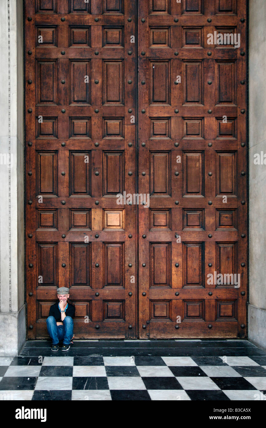 Happy young smiling man sitting in front of huge wooden doors gate St ...