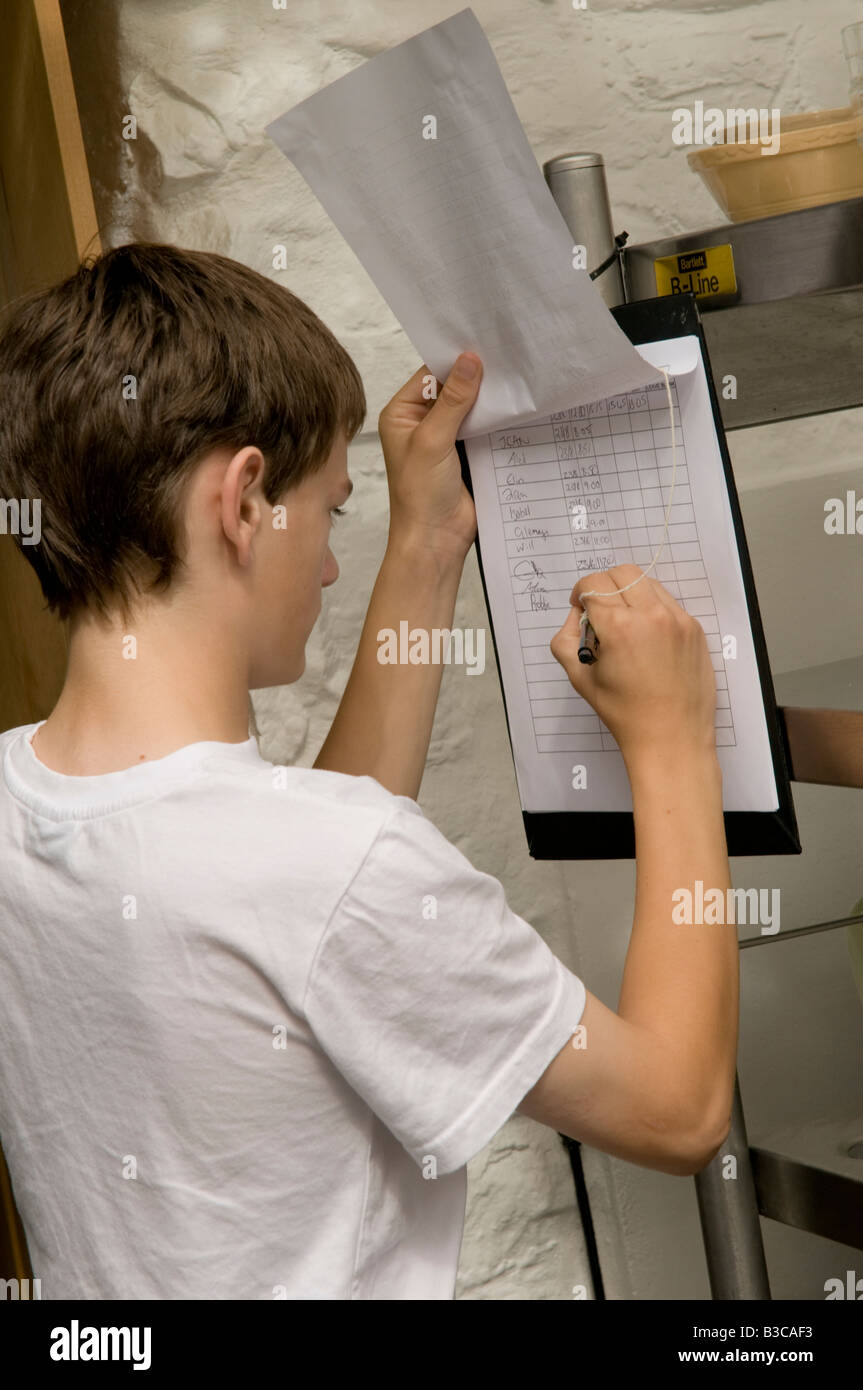Young teenage boy employed in summer holiday job, filling in his working hours on timesheet in a restaurant kitchen, UK Stock Photo