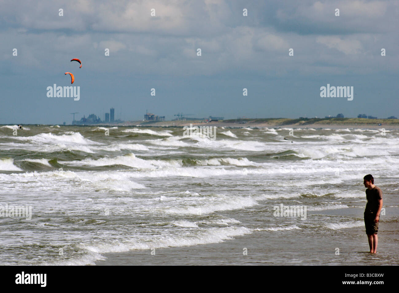 Man standig in sea stormy wather high wind huge waves kite flying Den Haag in background distance beach Hoek van Holland Stock Photo