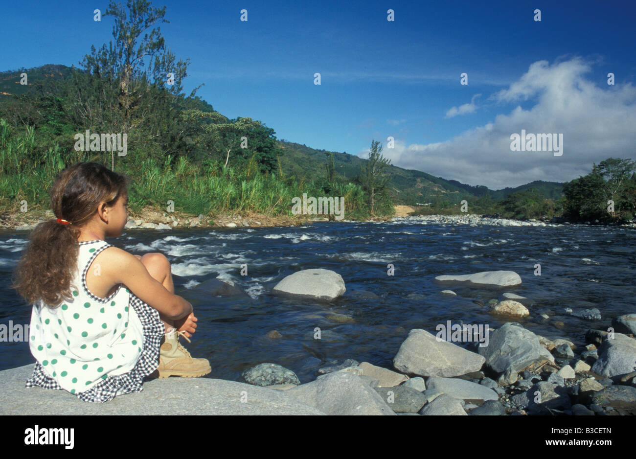 Little Girl Sitting Beside River in Rio Reventazon Orosi Valley Central VAlley Costa Rica Central America Stock Photo