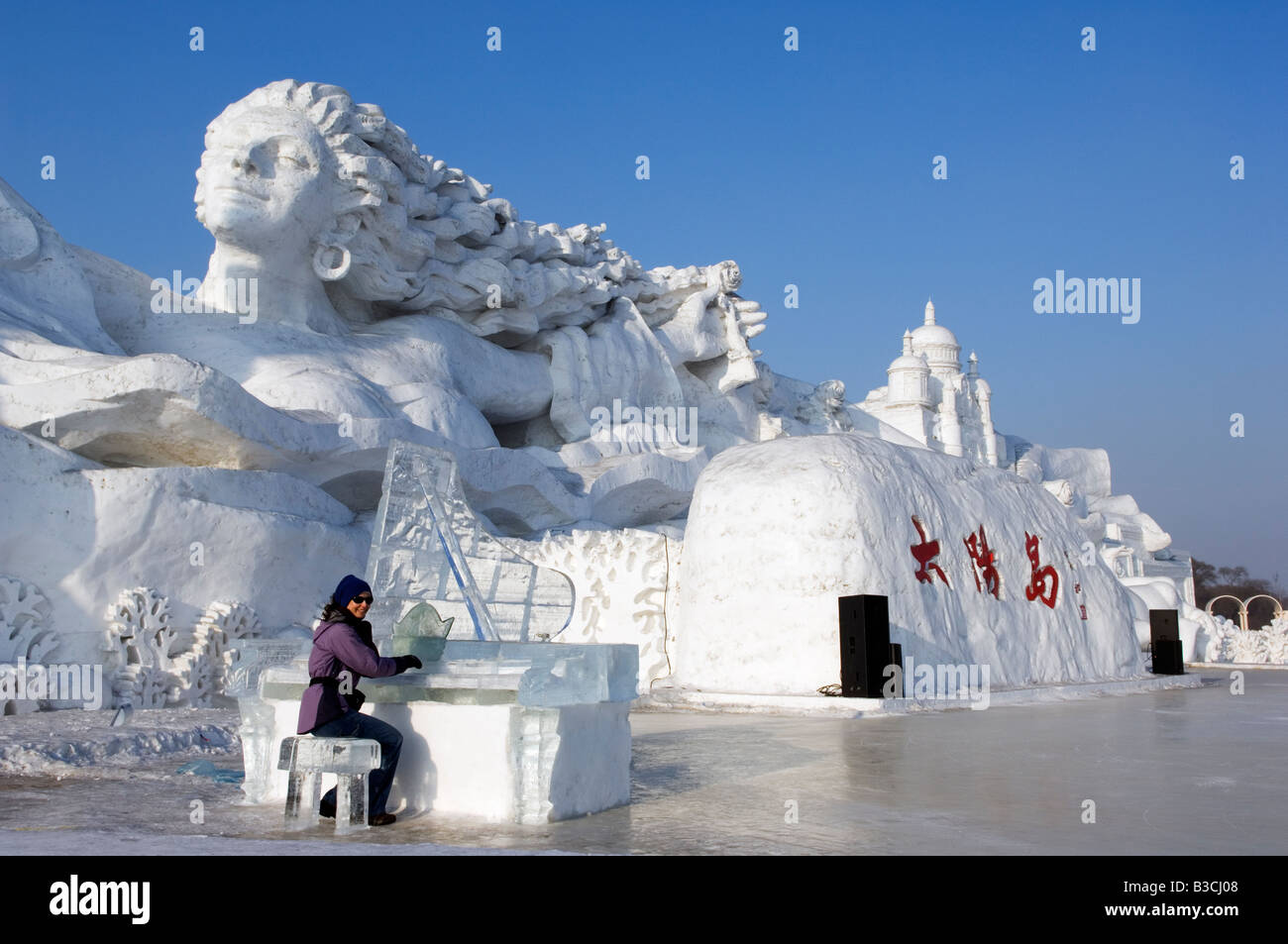 China, Northeast China, Heilongjiang Province, Harbin City. Snow and Ice Sculpture Festival at Sun Island Park. A tourist is playing a sculpted ice piano in front of giant snow sculptures. Stock Photo