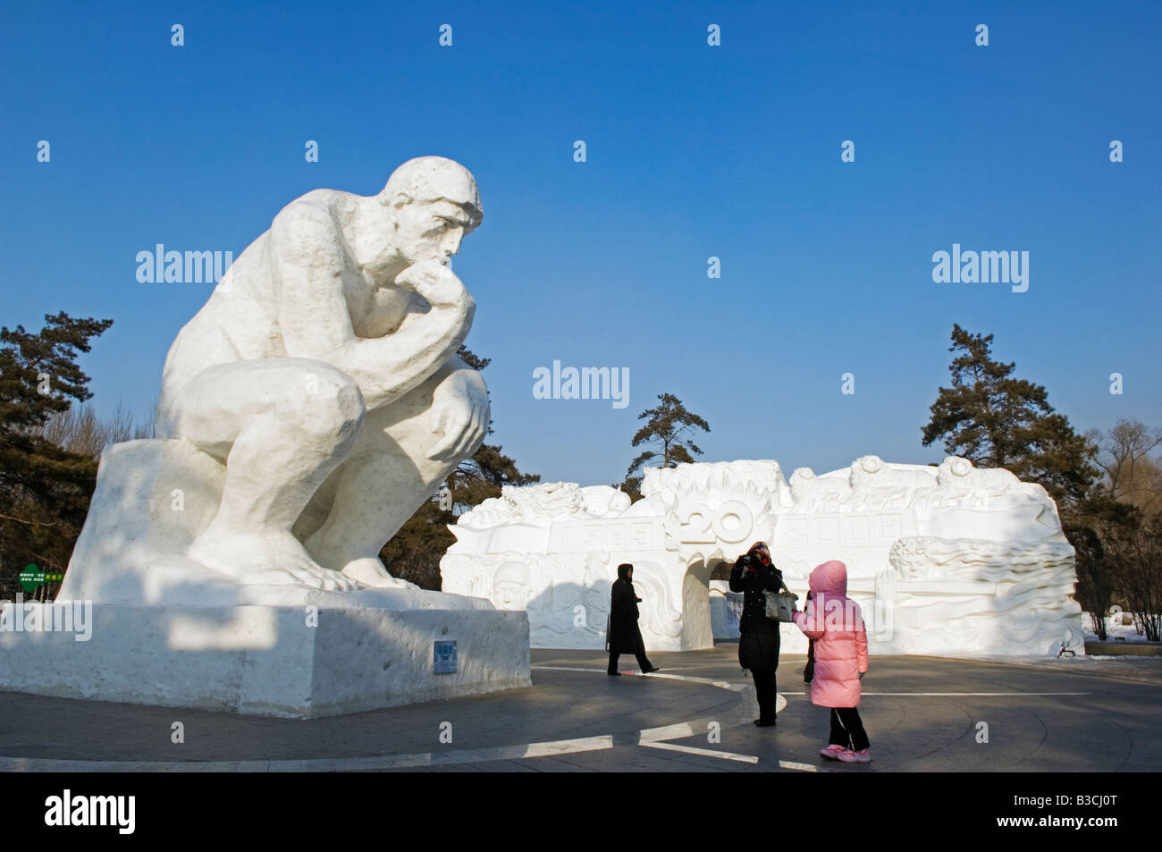 China, Northeast China, Heilongjiang Province, Harbin City. Snow and Ice Sculpture Festival at Sun Island Park. Visitors standing beneath a thinking man sculpture. Stock Photo