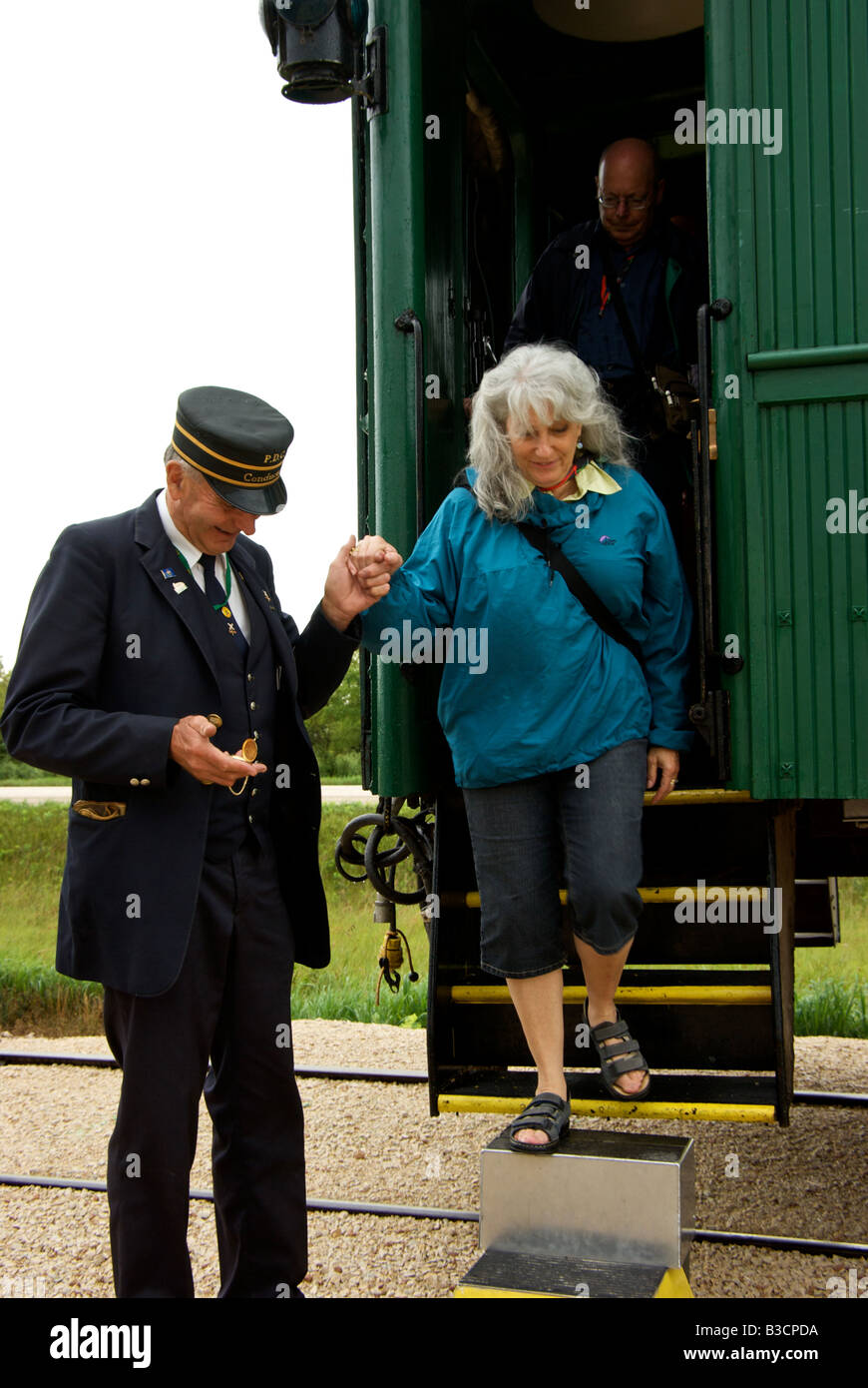 Prairie Dog Central antique railway volunteer conductor in period uniform helping a passenger debark from a wooden railway coach Stock Photo