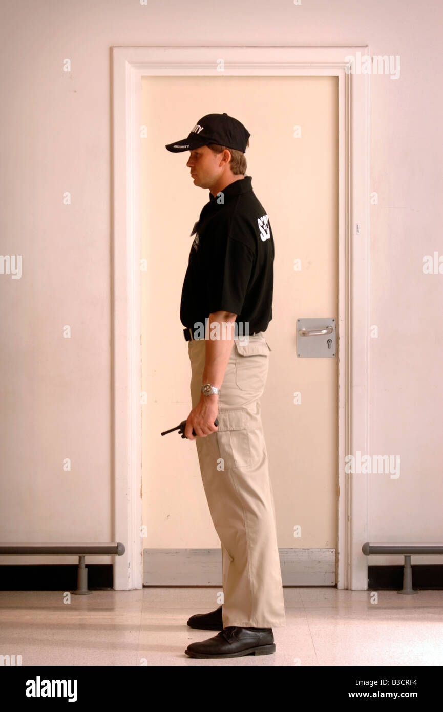 A SECURITY GUARD STANDS IN FRONT OF A DOOR HOLDING A WALKIE TALKIE UK