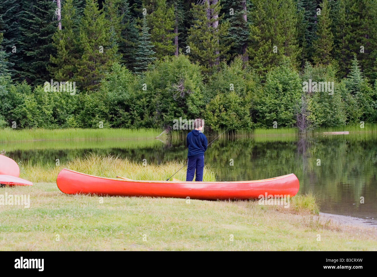 boy fishing in a lake beside his canoe - nice reflection of the trees in the water Stock Photo