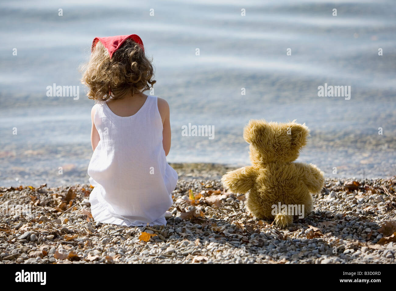 Germany, Bavaria, Ammersee, little girl (3-4) sitting on beach, rear view Stock Photo