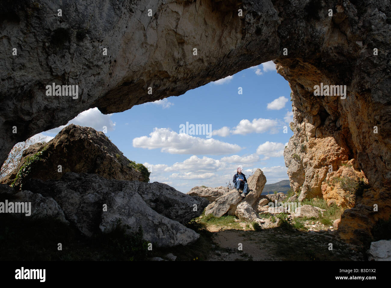 woman hiker sitting under Forada Rock Arch, Sierra de la Forada, Alicante Province, Comunidad Valenciana, Spain Stock Photo